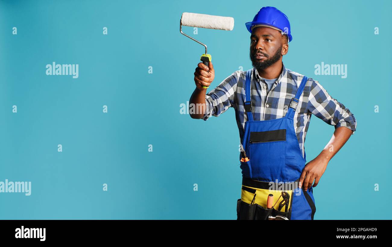Repairman in overalls painting walls with roller brush, using