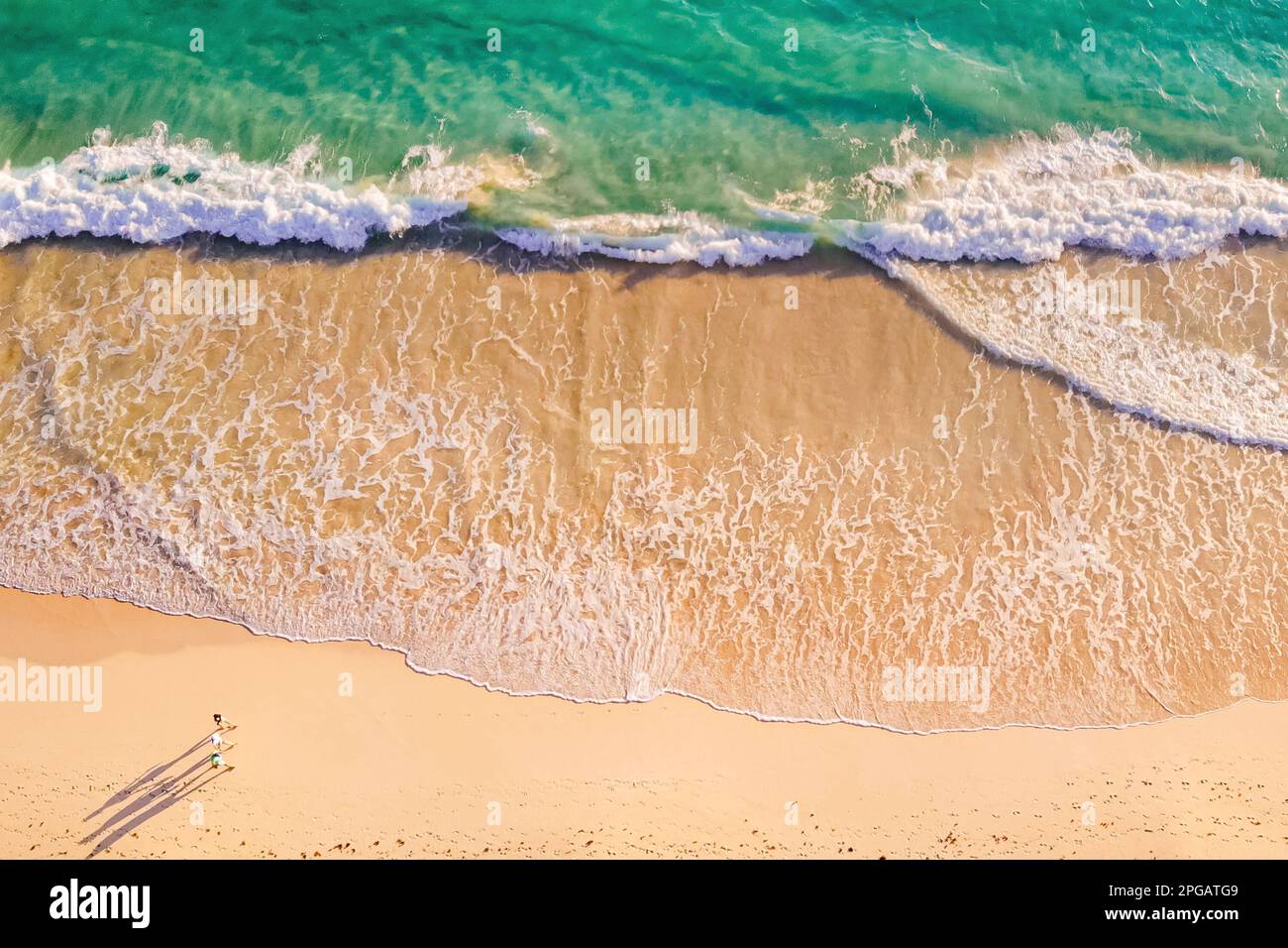 Walking along the coast of the ocean at sunrise. Beautiful summer aerial video. Overhead view of people walking by the white sandy beach along the amazing clear light blue ocean. Healthy lifestyle Stock Photo