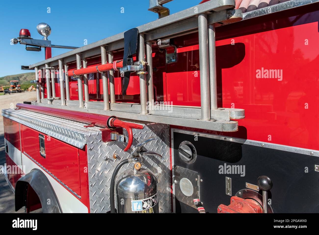 Beaching fire pick ax and sturdy extension ladder is firmly secured to the side of the red fire truck. Stock Photo