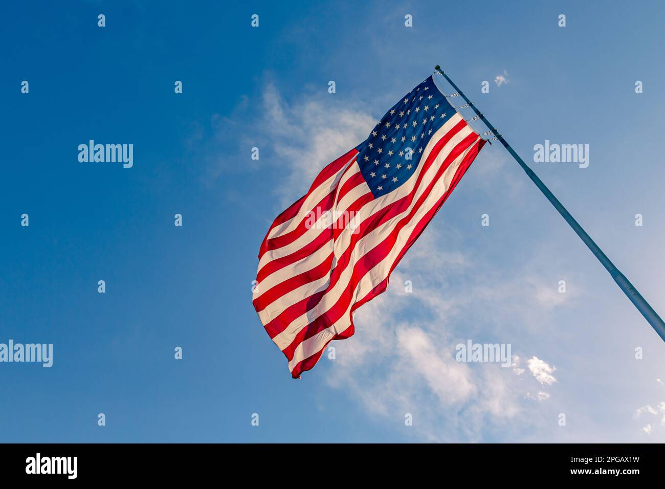 American USA flag on a flagpole waving in the wind. USA Flag Waving United States of America Flag Flying. American flag flying high on a pole against blue sky background on a clear day Stock Photo
