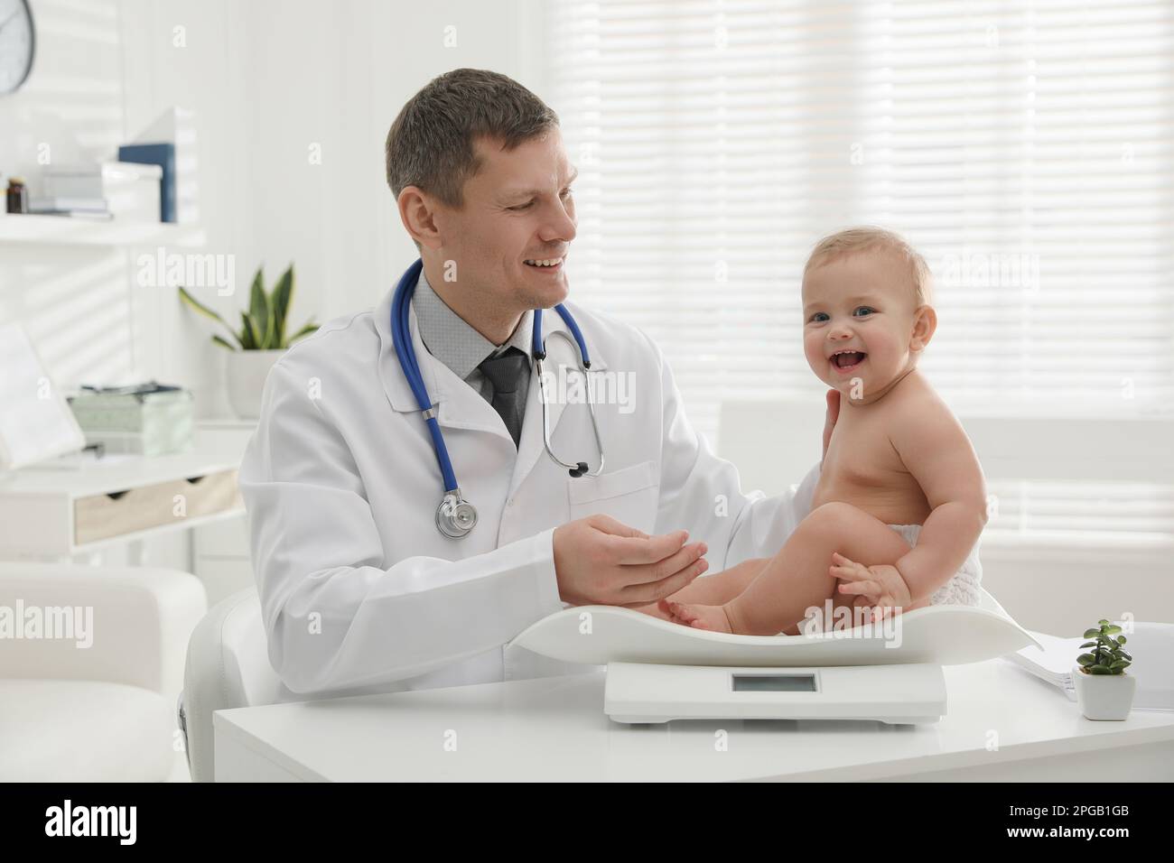 Pediatrician weighting cute little baby in clinic Stock Photo