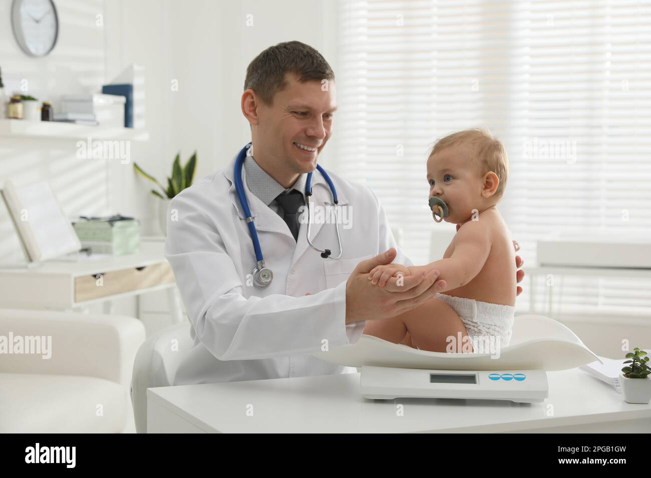 Pediatrician weighting cute little baby in clinic Stock Photo