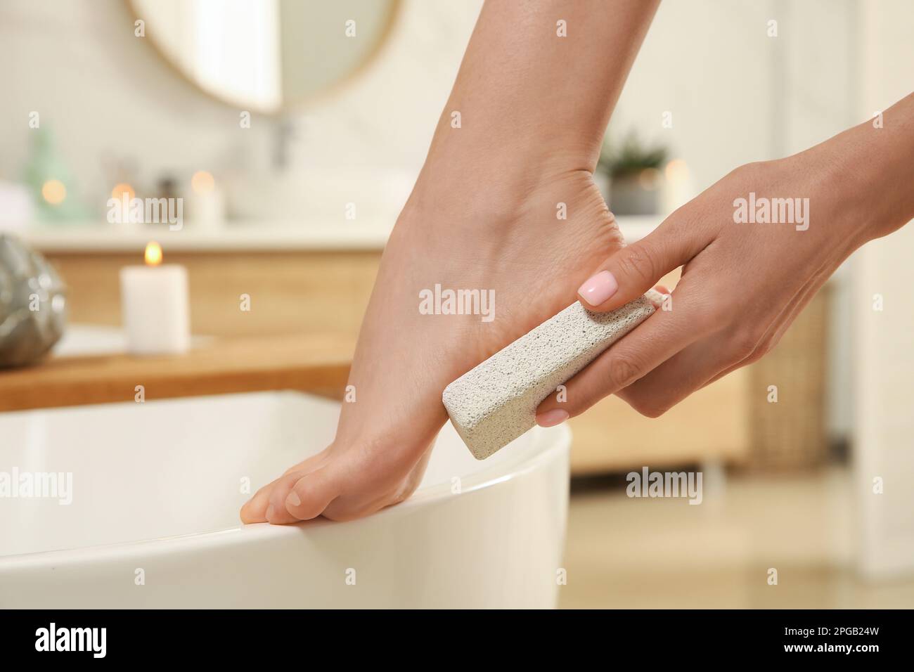 Woman using pumice stone for removing dead skin from feet in bathroom