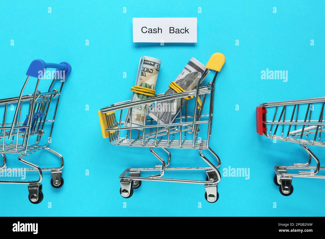 Card with word Cashback, rolled dollar banknotes and shopping carts on