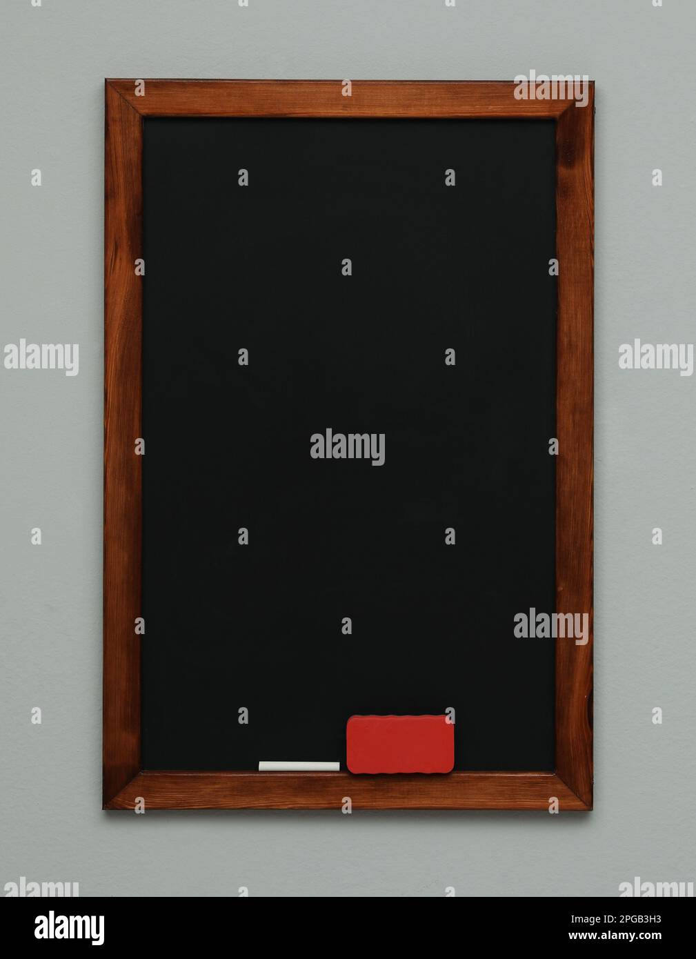 Clean blackboard with chalk and duster hanging on grey wall Stock Photo