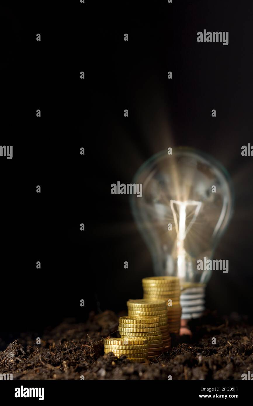 Rising piles of coins with lighted light bulb on black background ...