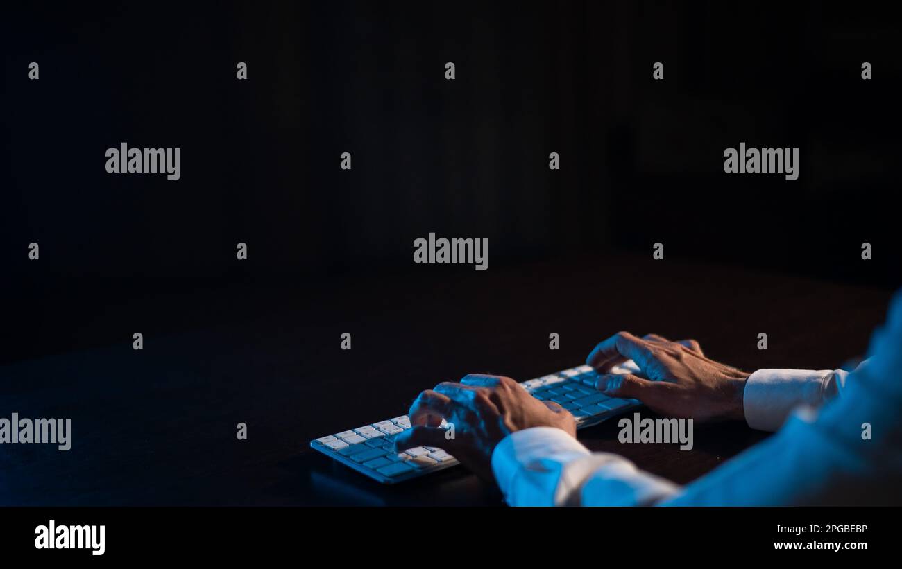 Close-up of male hands on a keyboard in the dark.  Stock Photo