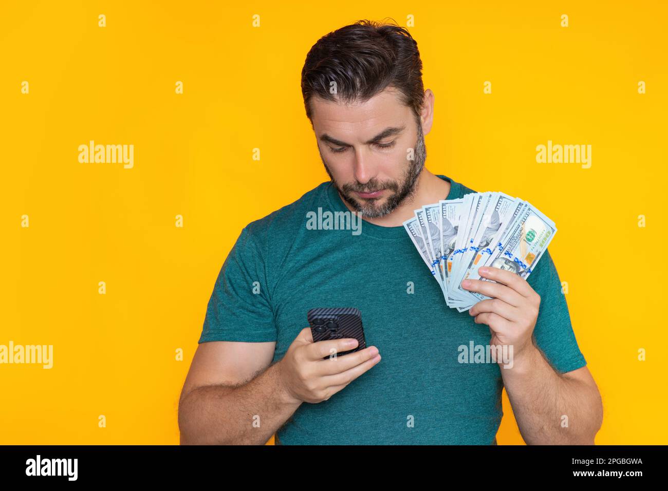 Man holding cash money in dollar banknotes on isolated yellow background. Studio portrait of business man with bunch of dollar banknotes. Dollar money Stock Photo