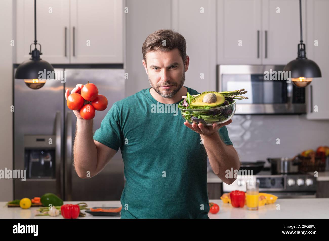 Handsome man cooking salad in kitchen. Guy cooking on kitchen with vegetables. Portrait of casual man cooking in the kitchen with vegetable Stock Photo