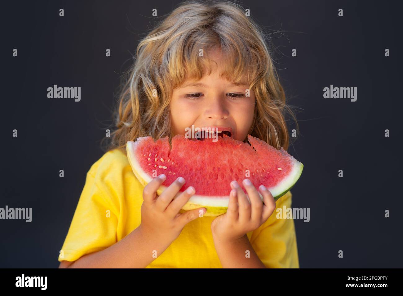 Kid face and watermelon, close up. Cute child eat watermelon. Kid is picking watermelon on gray background. Stock Photo