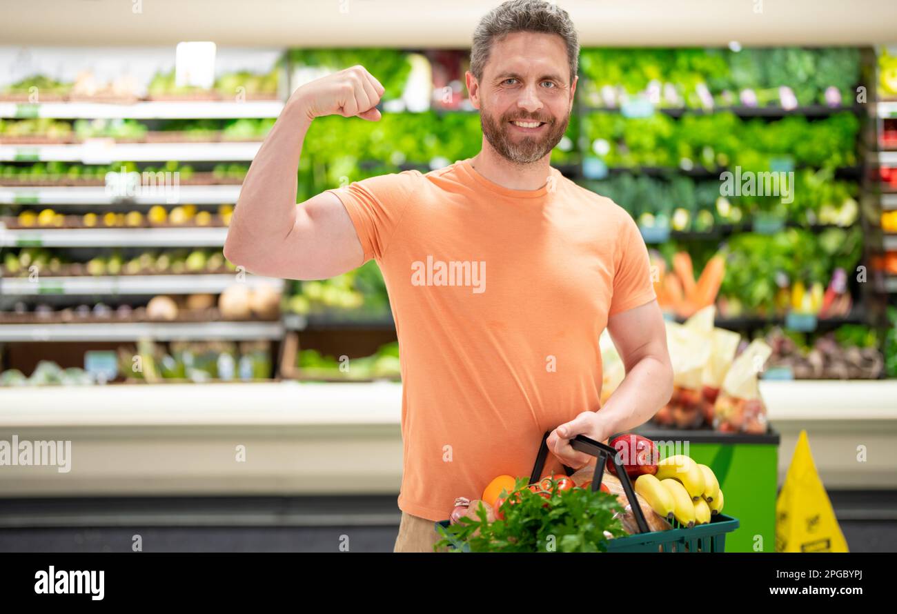 Man with shopping basket full of vegetables and fruits. Middle aged millennial man in a food store. Supermarket shopping and grocery shop concept. Man Stock Photo