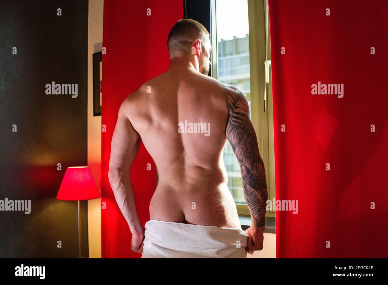 Handsome nude man in a bedroom. Young sexy man at night. Muscular handsome man in hotel room on window curtains. Shirtless topless sexy male model Stock Photo