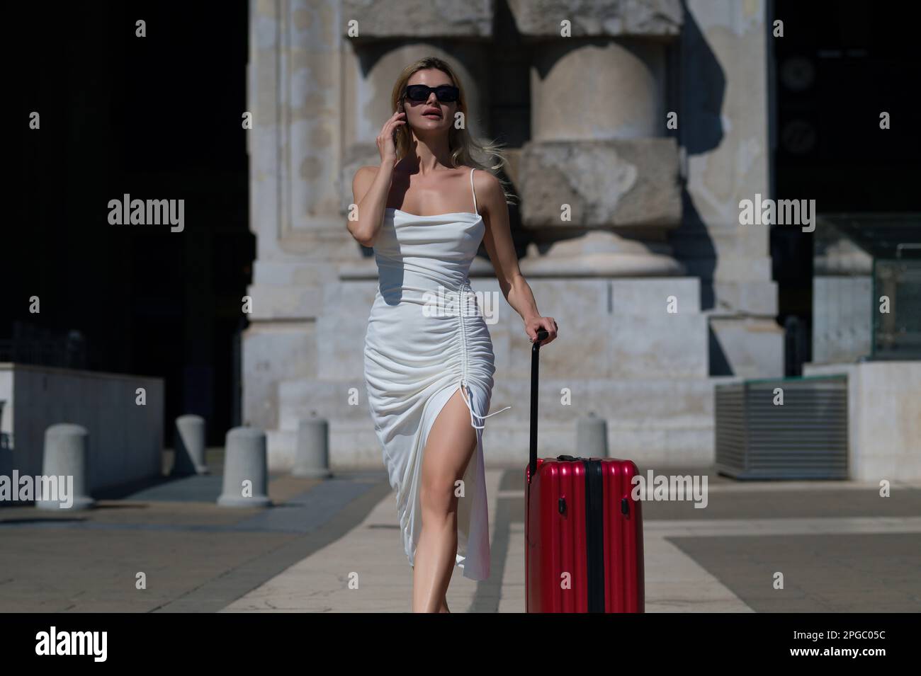 Fashion woman with suitcas going on vacations. Travel lifestyle. Sexy young girl on business trip walking with luggage on street. Stock Photo