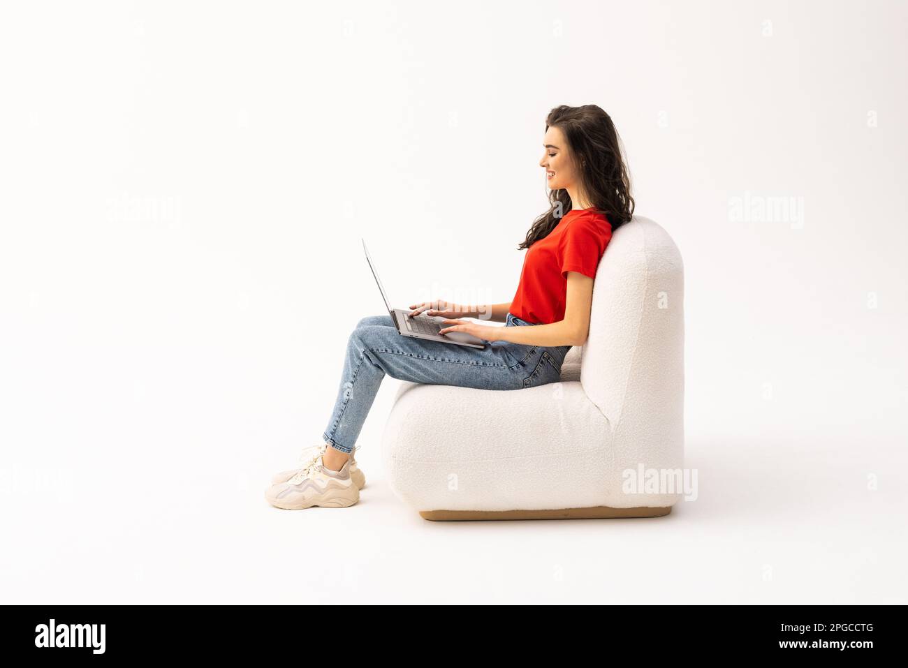 Portrait of a smiling young businesswoman sitting in a chair with laptop computer against white background Stock Photo