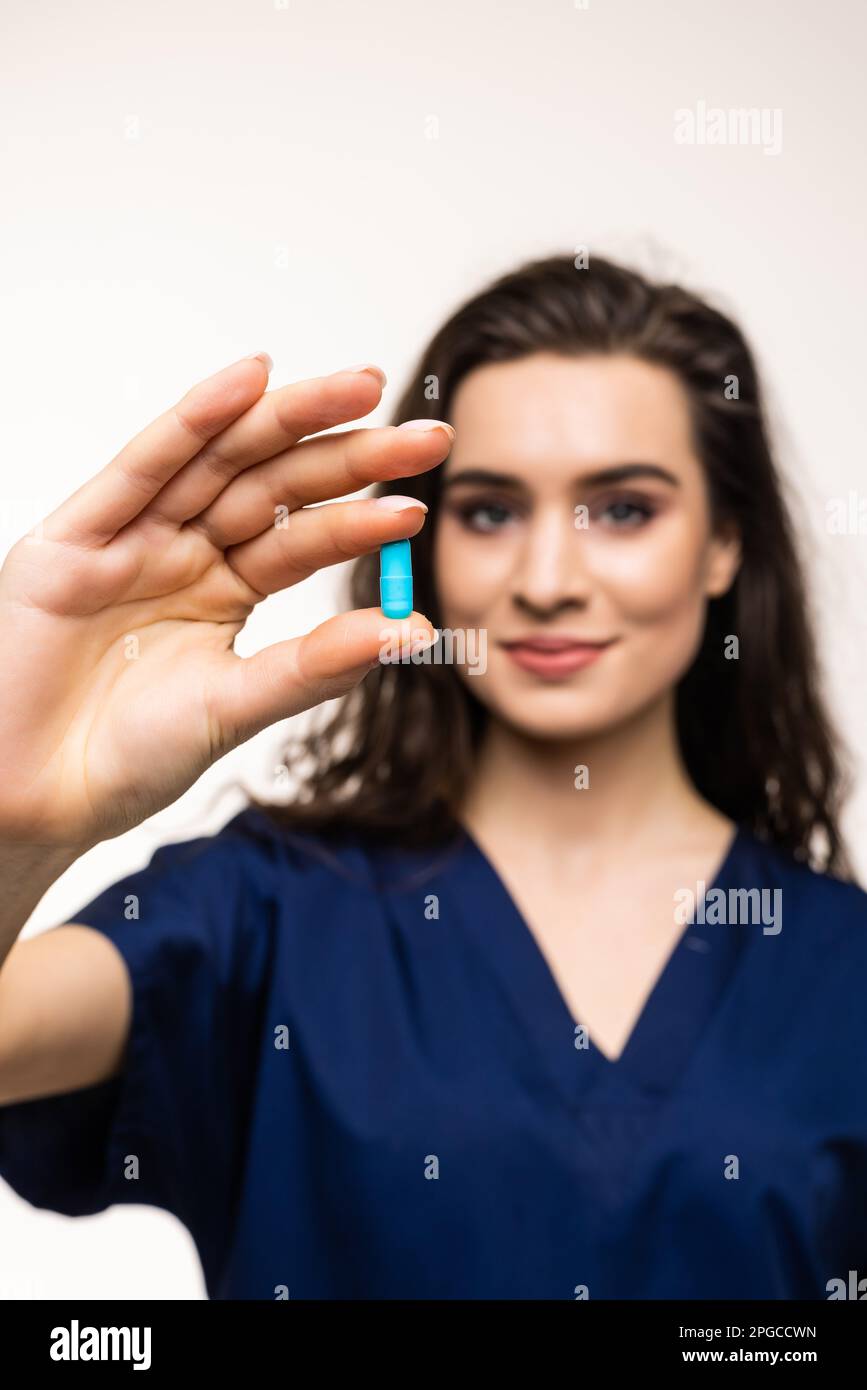 Pointing at pills. Portrait of young woman, doctor, therapeutic or medical advisor wearing face mask and blue uniform on white background. Concept of Stock Photo