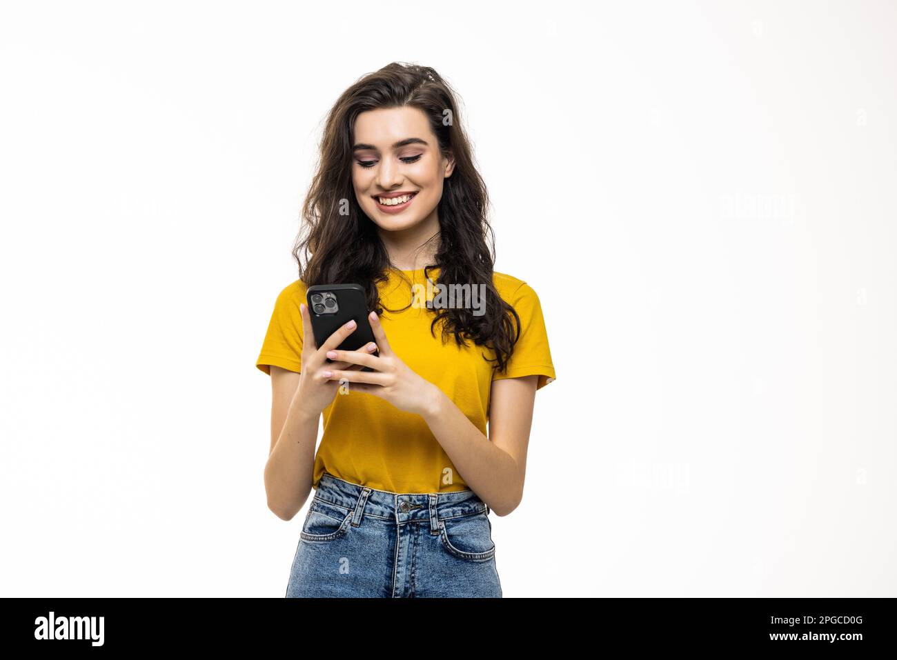 Young brunette woman smiling while using cellphone isolated over white background Stock Photo