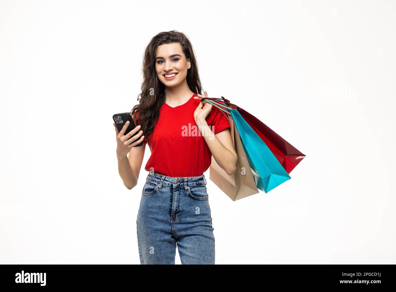 Portrait of a pretty casual girl holding shopping bags while using mobile phone isolated over white background Stock Photo