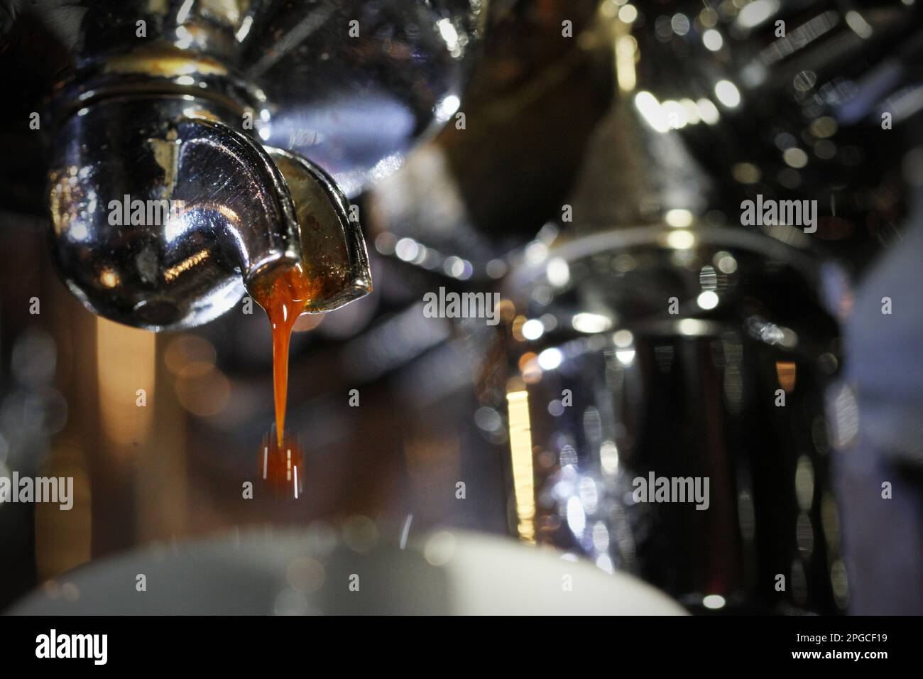 Extreme close up of the start of the perfect espresso pour with the brown coffee shot dripping off the stainless steel single portafilter handle. Bari Stock Photo