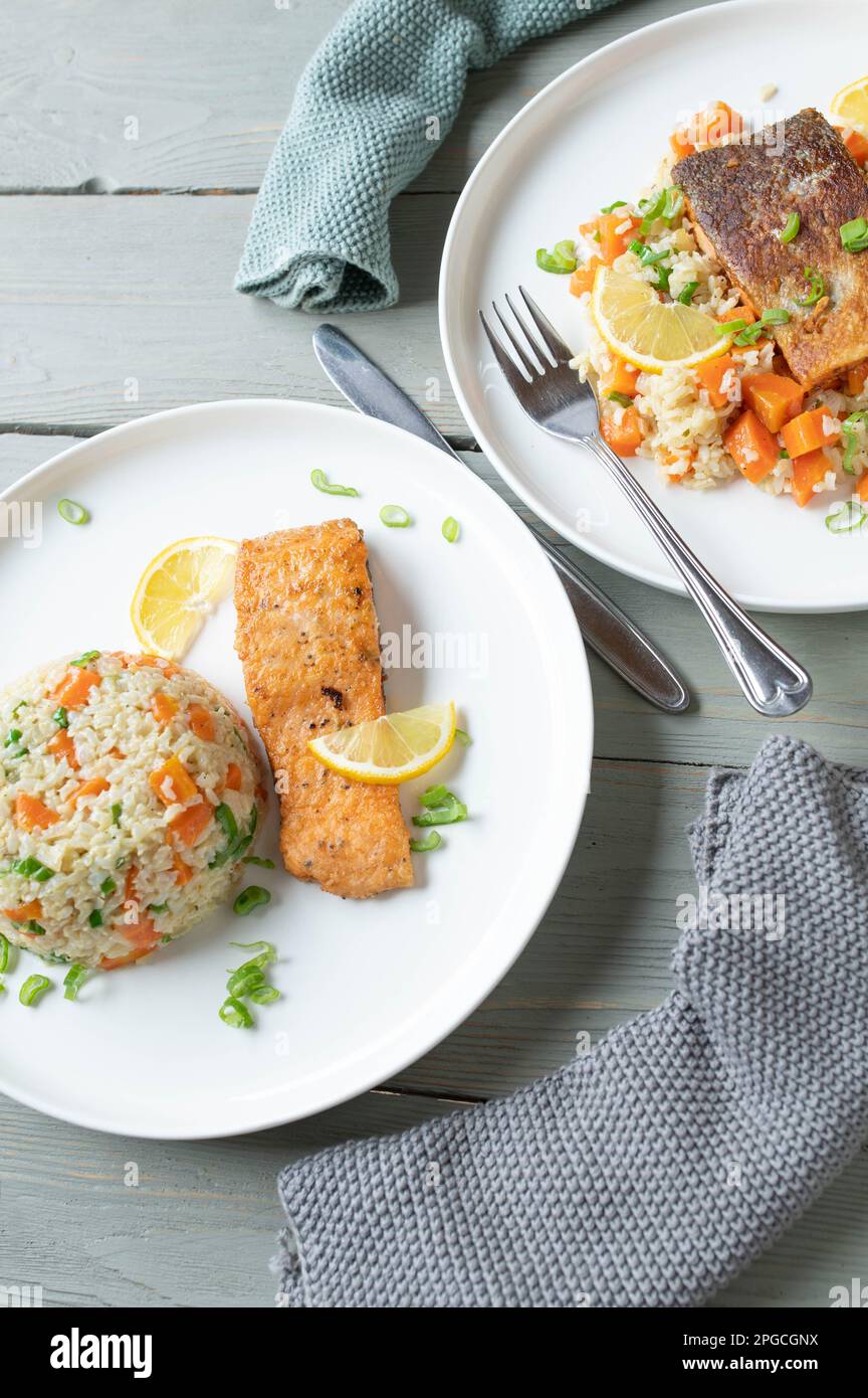 Pan fried salmon fillet with brown rice and vegetables on plates with two serving variations Stock Photo