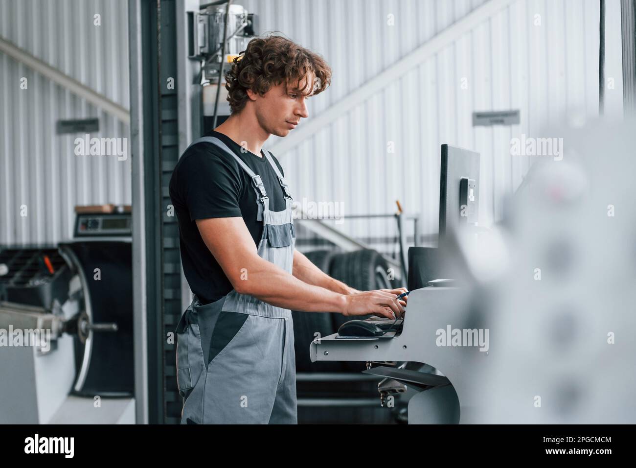 Auto Mobile Stylist Computer Using computer. Adult man in grey colored uniform works in the ...