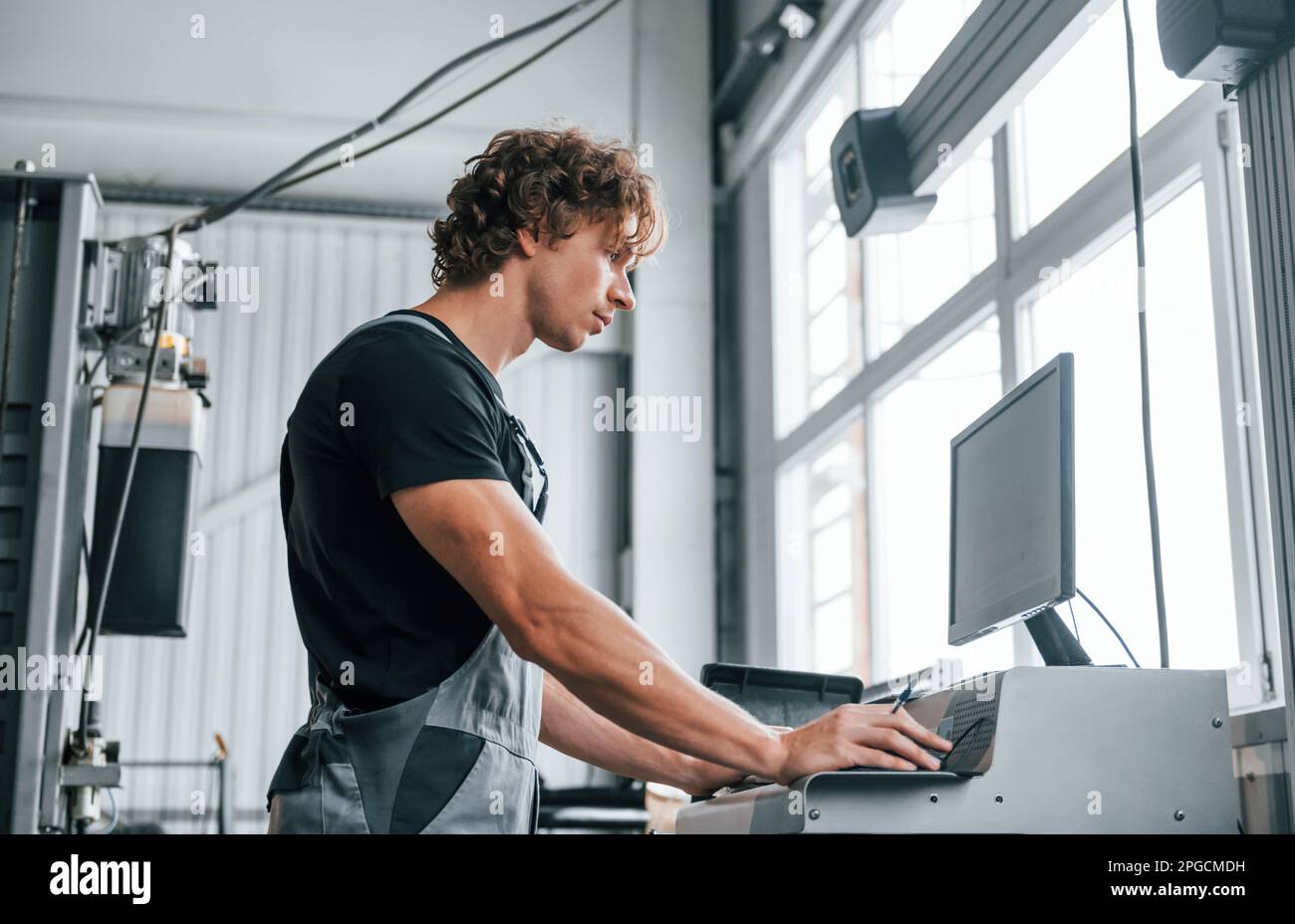 Using computer. Adult man in grey colored uniform works in the automobile salon Stock Photo