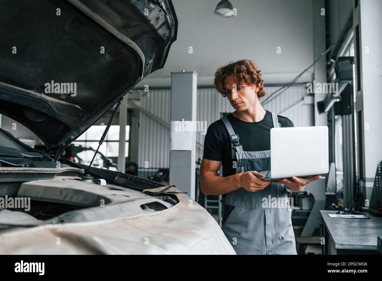 Auto Mobile Stylist Computer Using computer. Adult man in grey colored uniform works in the ...