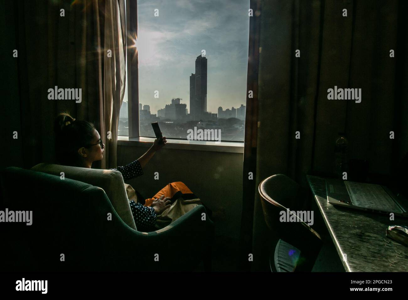 JAKARTA, INDONESIA - March 21, 2023: A woman with her cell phone inside a hotel room in the Jakarta area, Indonesia, on March 21, 2023. Stock Photo