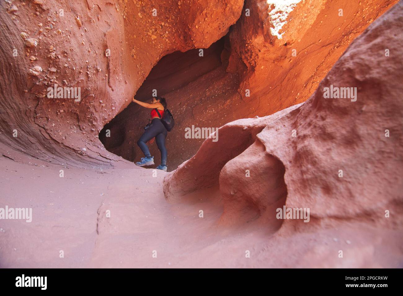 From below of female tourist in casual clothes with backpack leaning on wall while exploring famous Red Canyon Stock Photo