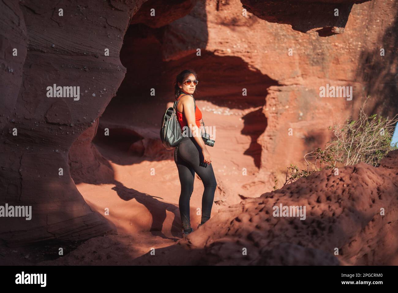 Full body back view of female tourist in casual clothes and sunglasses looking at camera with backpack exploring famous Red Canyon Stock Photo