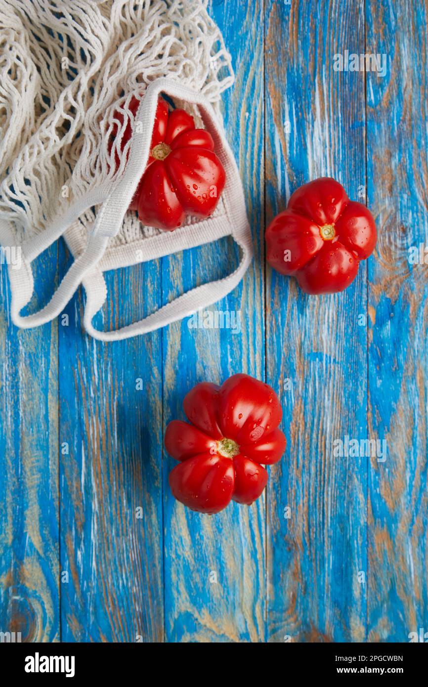 Top view of fresh ripe red tomatoes with eco friendly cotton mesh bag placed on blue stripped wooden table Stock Photo
