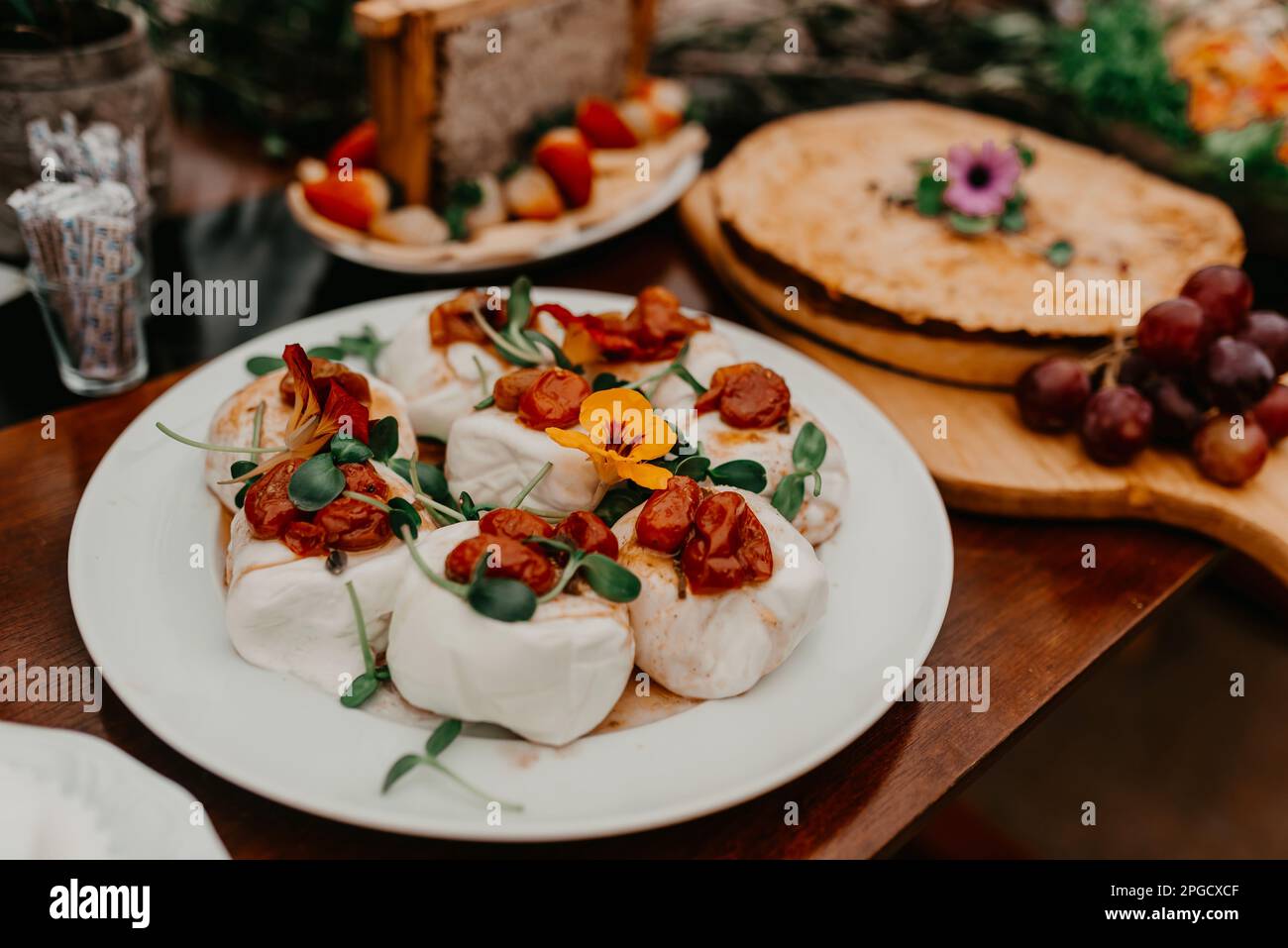 A wooden table top decorated with a delicious spread of food including two pizzas, various fruits, and other condiments Stock Photo