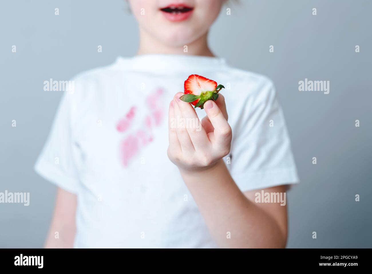 Child's hand holding a sliced strawberry and spilling juice on white t