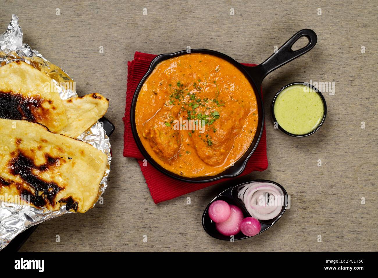 Top view of butter chicken served with naan pickled onion and mint