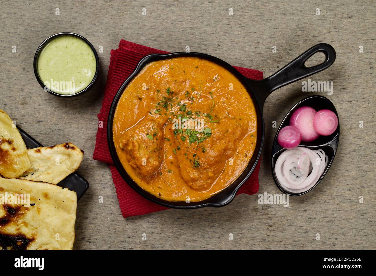 Top view of butter chicken and naan served with mint chutney and onion