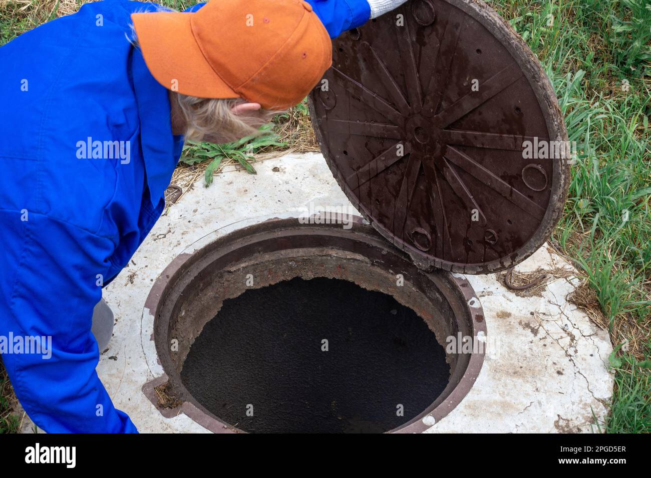 A worker opens the manhole cover and looks down into the well. Plumbing ...