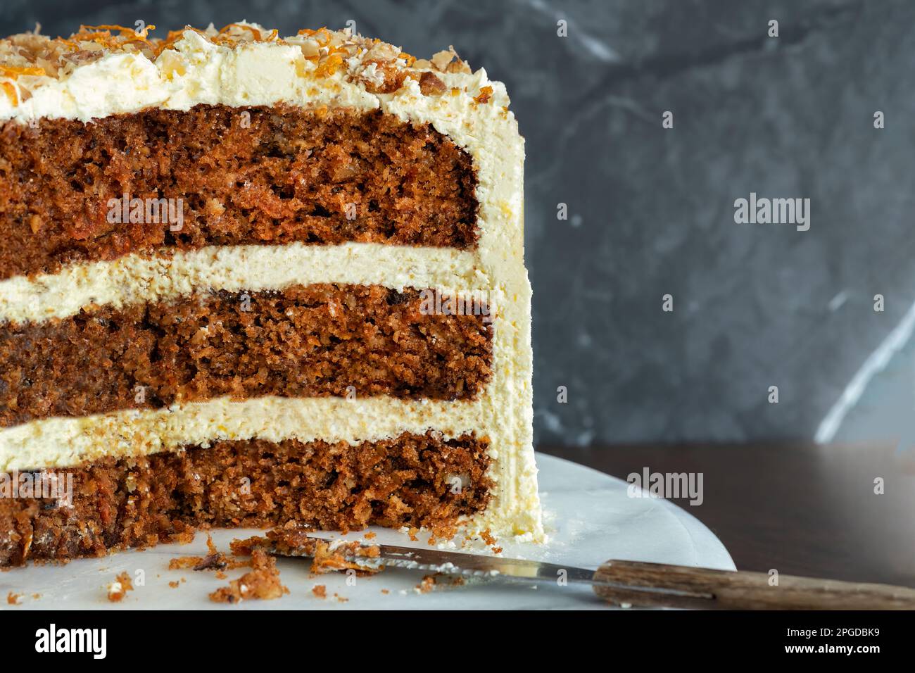 A three tiered traditional home baked carrot cake. The cake has a cream cheese frosting decorated with walnuts. The cake is cut showing the crumb Stock Photo