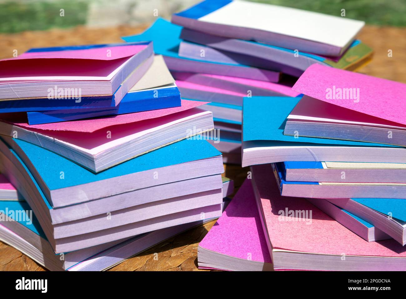 Many cheap small notepads in 3 messy stacks seen from a side. A pile of