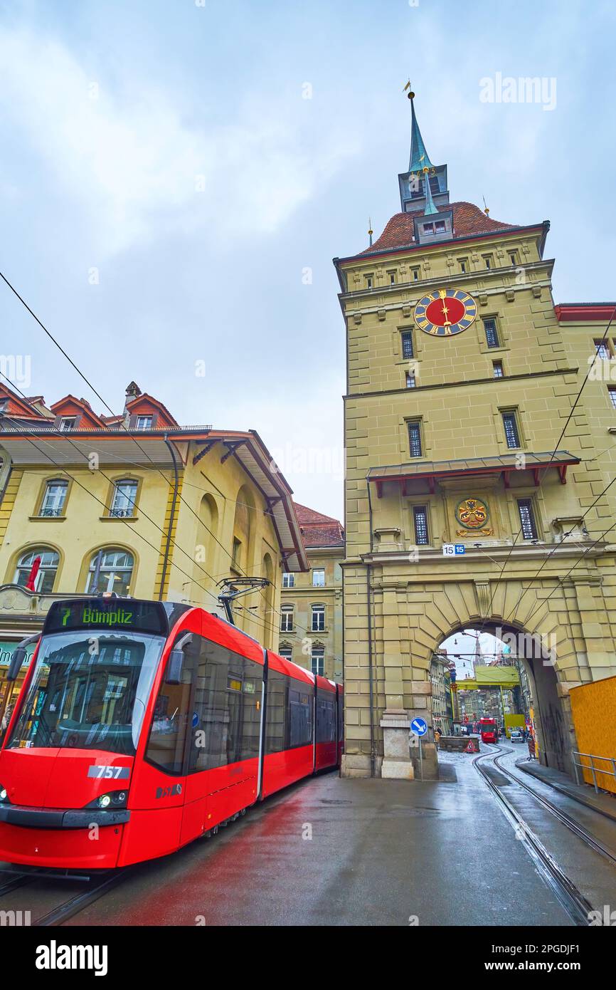 BERN, SWITZERLAND - MARCH 31, 2022: Modern red tram rides on Waisenhausplatz next to medieval Kafigturm tower, on March 31 in Bern, Switzerland Stock Photo