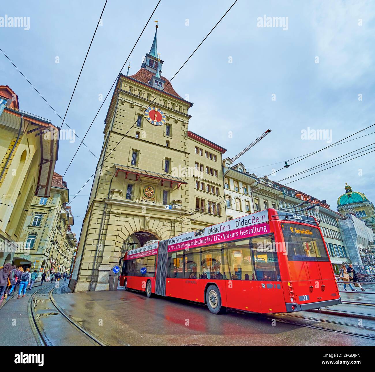 BERN, SWITZERLAND - MARCH 31, 2022: Red trolleybus driving through the arched portal in Kafigturm tower on Waisenhausplatz square, on March 31 in Bern Stock Photo