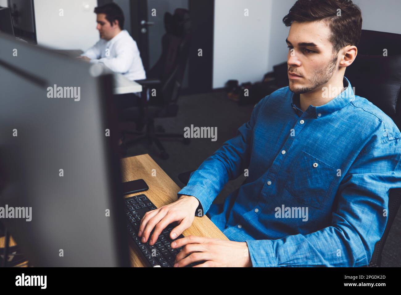 Young man in a blue shirt a programmer typing on keyboard while looking at the computer screen, coding  Stock Photo