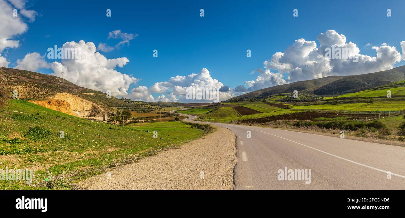 A Scenic Drive Through Mountains and Green Fields Under a Blue Sky with Clouds in Tunisia Stock Photo