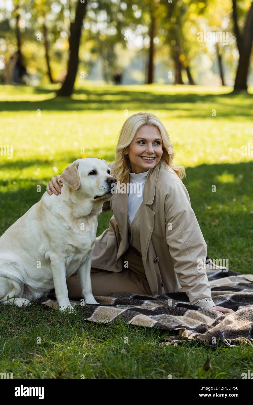 happy middle aged woman with blonde hair cuddling labrador dog while ...