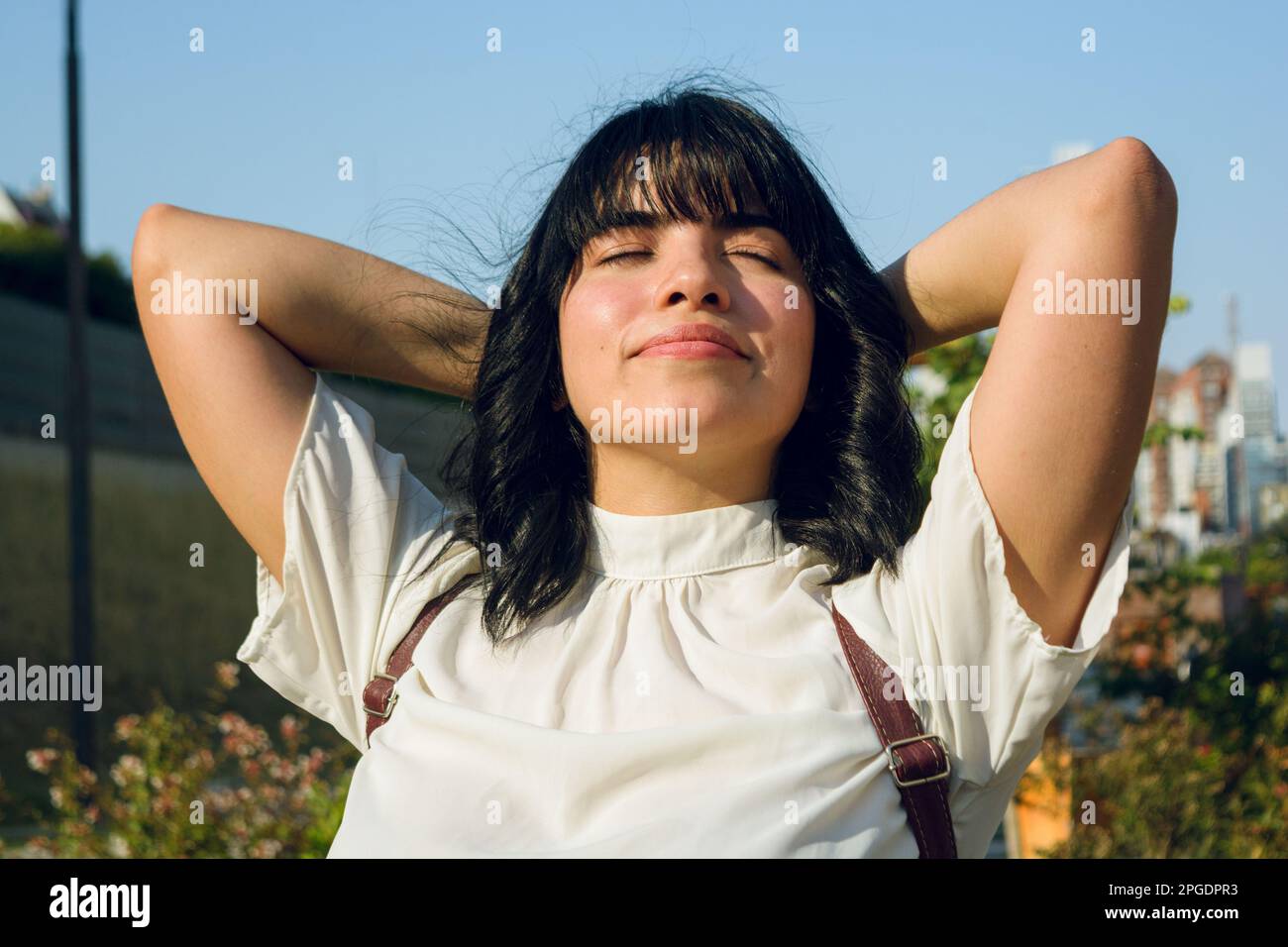 break from long class at university, young woman outdoors, sitting with arms behind head and eyes closed, relaxed and breathing. Stock Photo