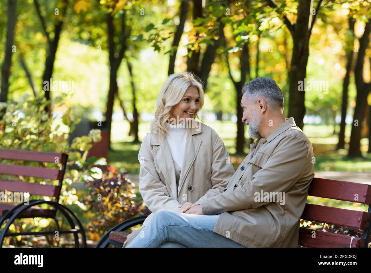 cheerful middle aged couple talking while sitting on bench in green park,stock image Stock Photo