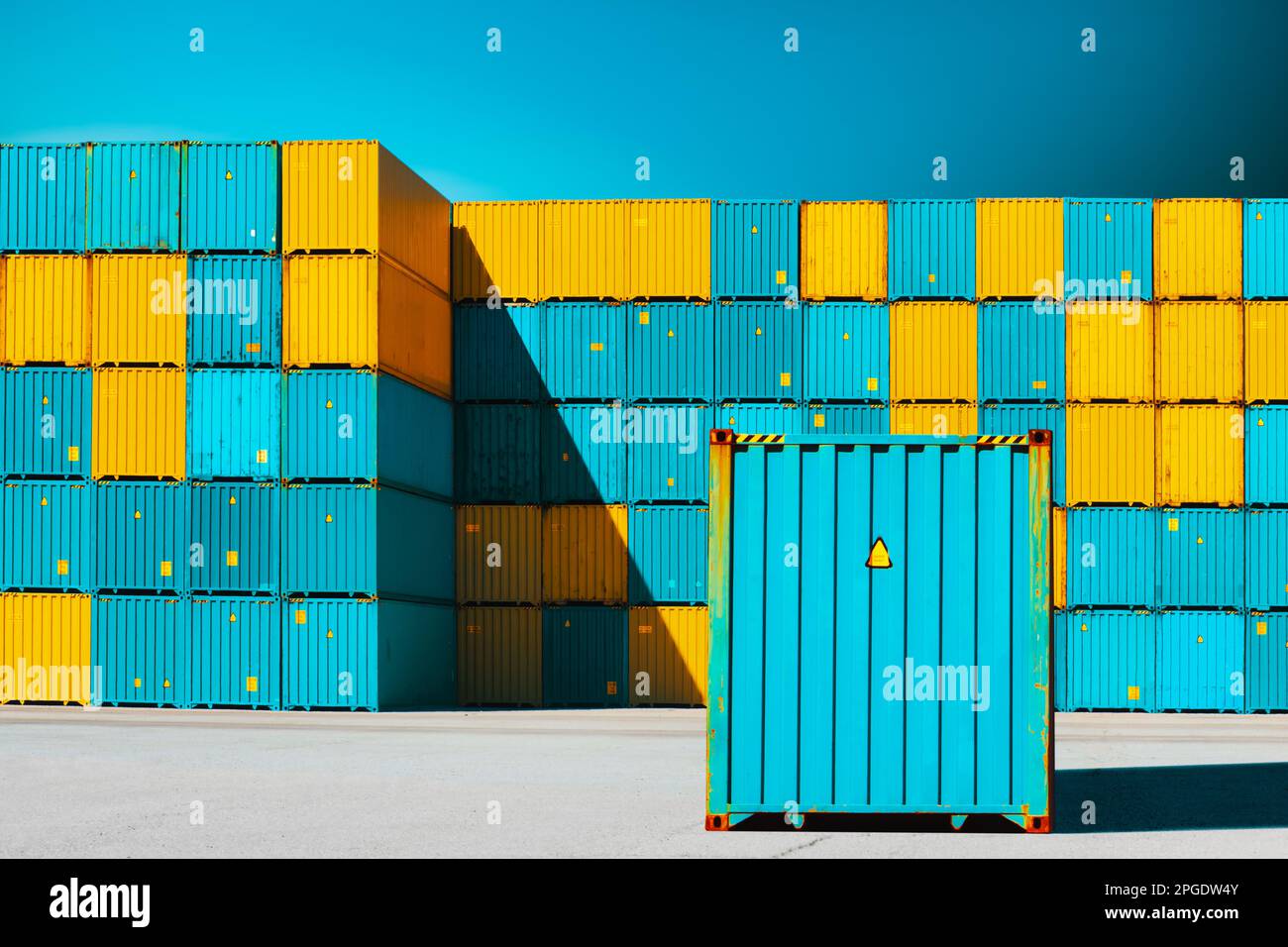 Lone shipping container in front of a stack of blue and yellow shipping containers Stock Photo