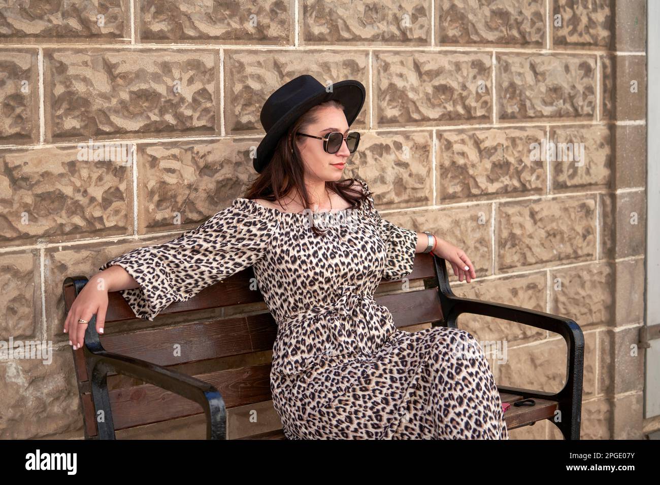 Young girl in leopard dress, black hat and sunglasses posing in the park Stock Photo