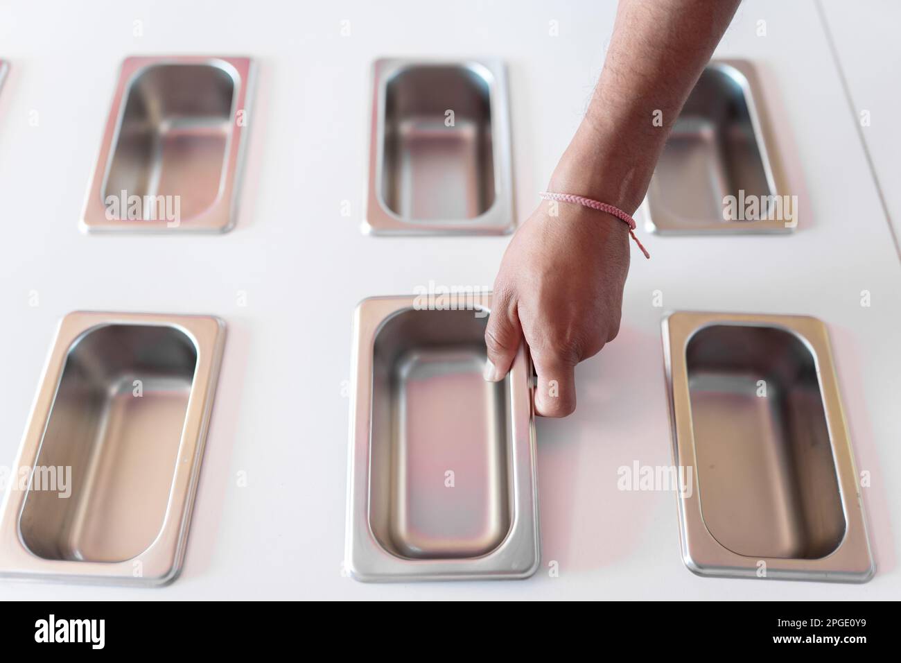 A hand of an ice-cream parlor worker is placing a clean metal tray Stock Photo