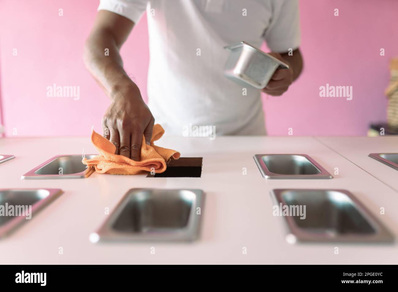 An icecream parlor worker is cleaning the shop counter with a cleaning