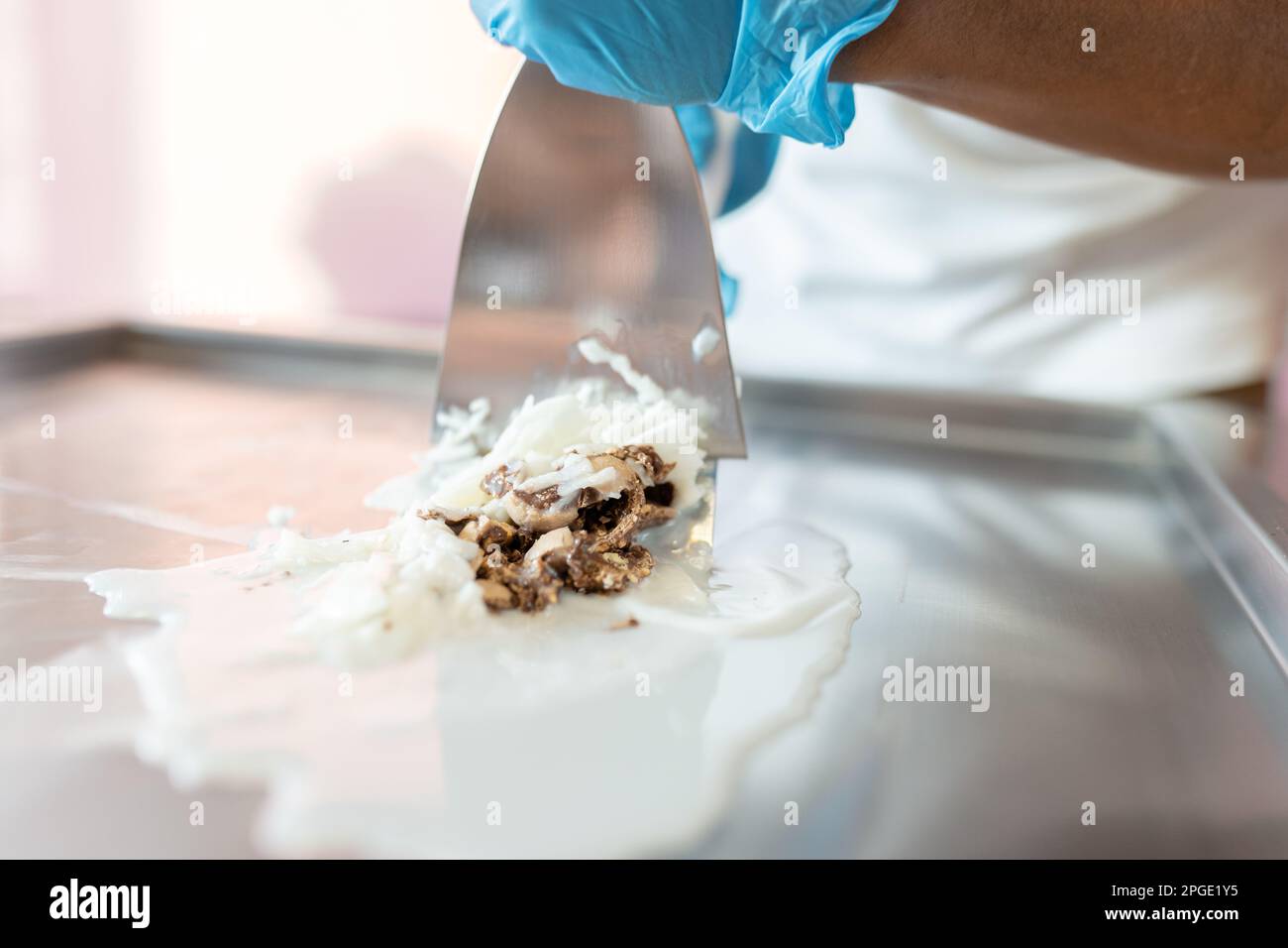 https://c8.alamy.com/comp/2PGE1Y5/a-worker-is-using-spatulas-to-mix-chocolate-striped-coconut-and-milk-on-a-rolled-ice-cream-machine-2PGE1Y5.jpg