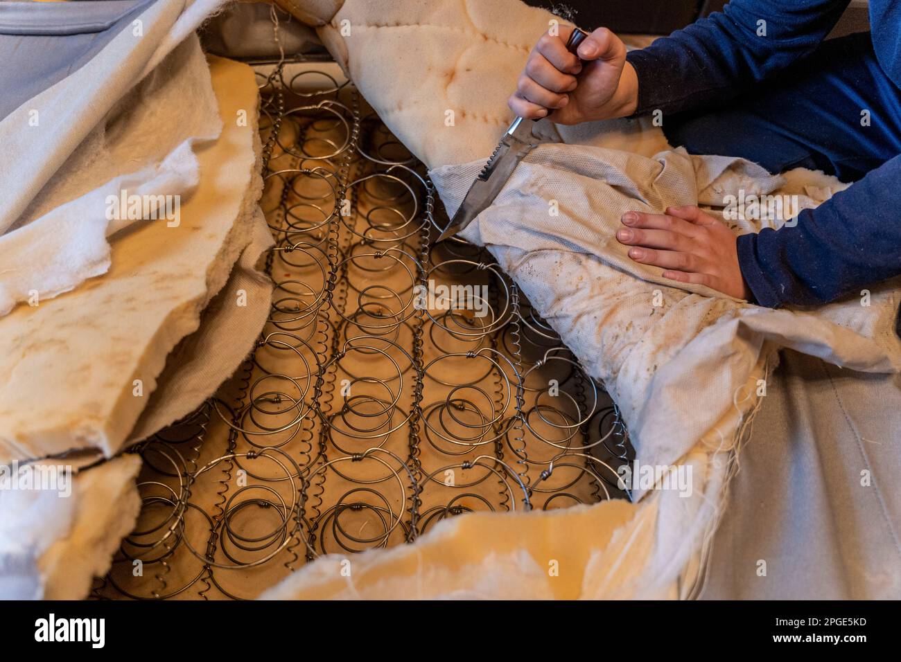 A man cut a spring mattress with a knife. Spring block and foam lining